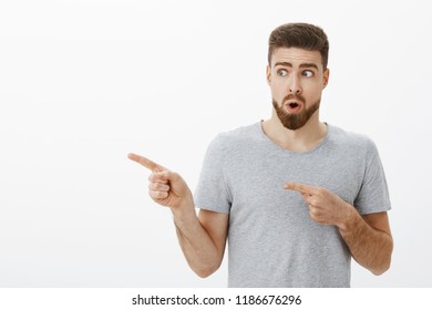 Portrait Of Curious And Amazed Good-looking Charming Male Model With Beard Holding Breat Folding Lips In Wow Sound Looking And Pointing Left At Cool Hairstyle Wanting Same One While In Barber Shop