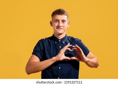 Portrait Of Curious Charming Guy Showing Heart Symbol On Yellow Background