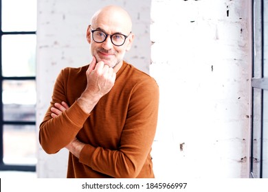  Portrait of curious man with beard and eyewear standing at the window. Hand on chin. - Powered by Shutterstock