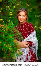 Portrait of a curly Beautiful girl in a red velvet dress and shawl posing in apple garden. Art work of romantic woman .Pretty tenderness model looking at camera.
