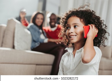 Portrait of curly cute child making call and laughing. Parents resting on background. Focus on daughter స్టాక్ ఫోటో