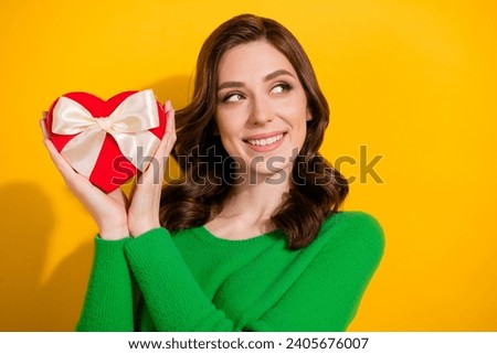 Portrait of curly lady in green pullover holding received giftbox heart with candies looks novelty isolated on yellow color background