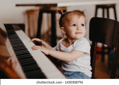 A Portrait Of A Cute 2-year-old Happy Baby Who Has Fun At The Piano Lesson. Little Child Girl Playing Piano In A Light Room. Selective Focus, Noise Effect