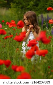 Portrait Of A Cute 6 Year Old Girl Wearing A White Summer Cotton Dress, Posing In The Poppy Field