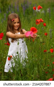 Portrait Of A Cute 6 Year Old Girl Wearing A White Summer Cotton Dress, Posing In The Poppy Field