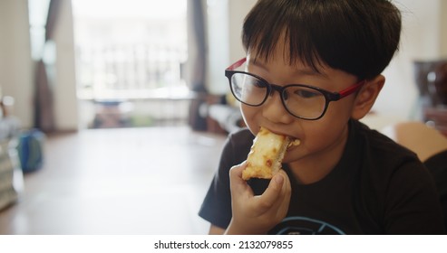 Portrait Cute Adorable Asian Kid Child Boy With Eyeglasses Enjoy Eating Bread Sticks At Home	