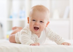 Portrait Of A Cute Adorable Baby Boy Wearing A Bodysuit Shirt Lying On Belly In Nursery Room