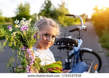 Portrait cute adorable caucasian blond little girl enjoy having leisure fun riding bicycle with family holding wild field flower at scenic rural country road on bright sunny day. Countryside vacation