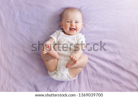 Portrait of cute adorable smiling laughing white Caucasian baby girl boy with blue eyes four months old lying on bed looking at camera. View from top above. Happy childhood lifestyle.