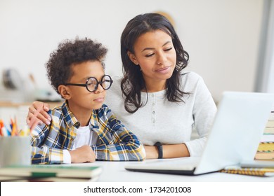 Portrait Of Cute African Boy Wearing Big Glasses While Using Laptop With Mom, Homeschooling And Remote Education Concept