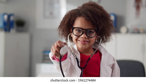 Portrait of cute african child doctor in white coat holding stethoscope in clinic office. Afro-american toddler girl as practitioner in uniform and glasses smiling at camera - Powered by Shutterstock