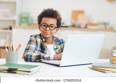Portrait of cute African-American boy using laptop and wearing big glasses while studying at home, remote education concept, copy space