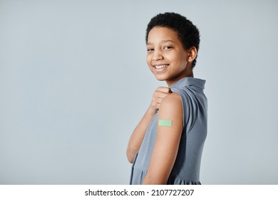 Portrait of cute African-American girl showing shoulder patch and smiling at camera after getting vaccinated, copy space
