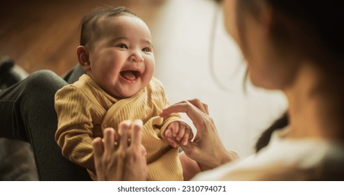 Portrait of a Cute Asian Baby Laughing, Resting on Her Mother's Lap and Enjoying a Bonding Time Together, Looking at her with Love. Playful Mom Tickeling her Toddler and Playing with Her. - Powered by Shutterstock