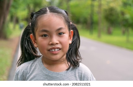 Portrait cute Asian child girl in the park, close up on the smiling face, some sweat drops on the face, gray color t-shirt, blurred background of trees in the park, sunlight image.