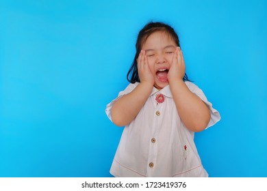 A Portrait Of A Cute Asian Girl Feeling Excited, Screaming With Her Eyes Closed And The Hands Covering Her Cheek With Plain Light Blue Background. 