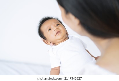 Portrait Of Cute Asian Newborn Baby Making A Sad Face And Pouting Before Starting To Cry While His Mother Holding His In Bedroom At Home. Mother Trying To Calm Down Crying Toddler Son.