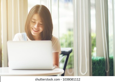 Portrait Of Cute Asian Teen Woman Using A Laptops Or Notebook Computer In Coffee Cafe. Bright And Light Process. Selective Focus. Filtered Image And Light Effect Added. Happy Smile Chill Out Concept