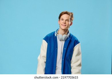 Portrait Of A Cute, Attractive, Handsome, Stylish Guy Listening To Music In Headphones While Standing Against A Light Blue Background. Studio Photography With Blank Space For Advertising Mockup