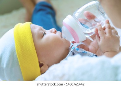 Portrait cute baby boy drinking water from bottle with his mom. Hand of asian young woman holding bottle with water while feeding aqua for her son. Lifestyle child concept.