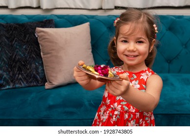 Portrait of cute baby girl holding candies from during Ramadan feast (aka: Ramazan or Seker bayrami). Sweets in little child hands as a tradition in middle eastern culture.