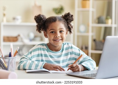 Portrait of cute black girl doing homework at desk and smiling at camera in home interior - Shutterstock ID 2253191033