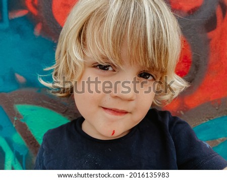 Portrait of a cute blonde caucasian child with stained face after been painting a graffiti 