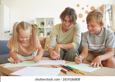 Portrait of cute blonde girl with down syndrome drawing with mother and brother together in home interior - Powered by Shutterstock