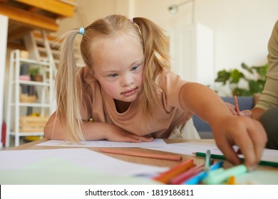 Portrait Of Cute Blonde Girl With Down Syndrome Drawing And Reaching For Pencils While Enjoying Development Class, Copy Space