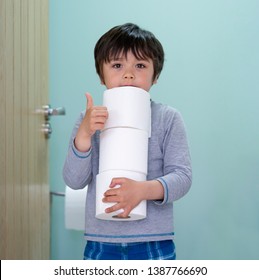 Portrait Of Cute Boy Holding Toilet Roll Standing In Front Of Toilet, Child With Smiling Face Showing Thumbs Up While Carrying A Stack Of Toilet Paper, 