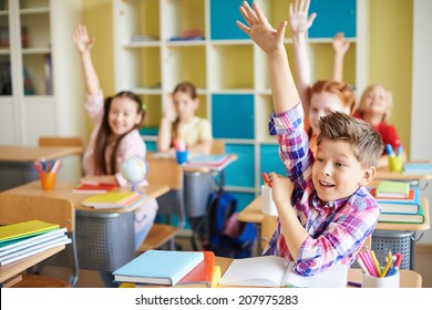 Portrait of cute boy raising hand at workplace with his classmates behind - Shutterstock ID 207975283