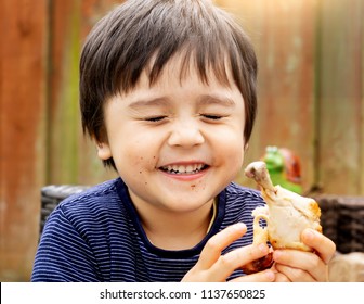 Portrait Of Cute Boy With Yummy Face Enjoy Eating Roasted Chicken Drumstick In The Garden, Happy Kid Eating Grilled Chicken, Healthy Picnic Food For Children Concept