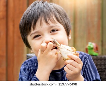 Portrait Of Cute Boy With Yummy Face Enjoy Eating Roasted Chicken Drumstick In The Garden, Happy Kid Eating Grilled Chicken, Healthy Food For Children Concept