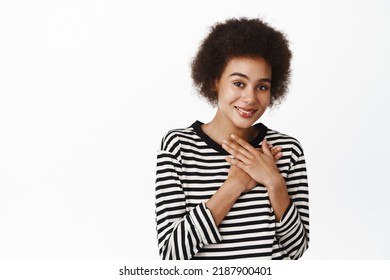 Portrait Of Cute Brunette African Girl Looking Humble And Grateful, Smiling Satisfied, Flattered, Holding Hands On Chest, White Background