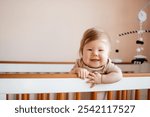 Portrait of a cute Caucasian baby girl 6 months old standing in a crib and looking at the camera. Copy space