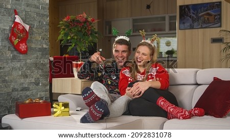 PORTRAIT: Cute Caucasian couple watching a fun holiday show on television on Christmas day. Beautiful young couple in love enjoying a fun Christmas movie TV on a couch in their decorated home