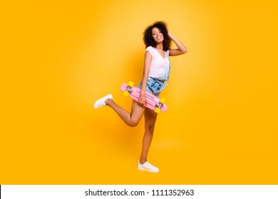 Portrait of cute cheerful coquette holding pink skate board in hand posing with raised leg enjoying weekend holiday isolated on yellow background - Shutterstock ID 1111352963
