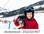 Portrait of cute confident adorable little kid boy enjoy having fun walking with ski at alpine mountain skiing resort on bright winter day. Toddler beginner skier rest of training in ski school