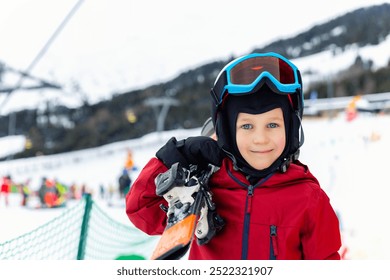 Portrait of cute confident adorable little kid boy enjoy having fun walking with ski at alpine mountain skiing resort on bright winter day. Toddler beginner skier rest of training in ski school