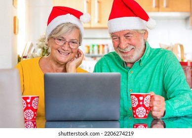 Portrait Of Cute Couple Of Mature Seniors Having Fun And Enjoying The Christmas Day Talking Online With A Laptop At Home With Some Old Friends.