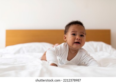 Portrait Of Cute Crying Black Little Baby Lying On Bed In Bedroom At Home, Closeup Shot Of Upset African American Infant Boy Or Girl Suffering Teething Or Demanding Attention, Copy Space