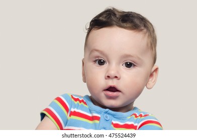 Portrait Of A Cute Curious Baby Boy Sitting Down. Adorable Six Month Old Child Happy Looking Surprised Raising His Eyebrow.