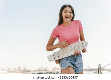 Portrait of cute emotional teenage girl holding skateboard having fun  looking at camera standing on the street. Positive lifestyle, summer concept - Powered by Shutterstock