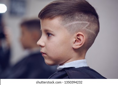 The Portrait Of A Cute European Boy In A Barbershop. He Is Getting His New Hairstyle With Hair Tatoo.