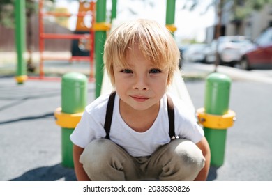 Portrait Of A Cute Four Year Old Boy On A Child Playground. He Is Crouched. Close Up.