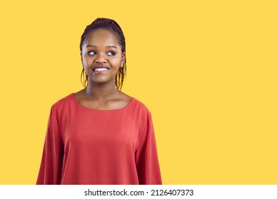Portrait of cute and funny unsure african american woman biting her lip on yellow background. Close up of young beautiful woman in red blouse looking away at copy space. Banner. Isolated.