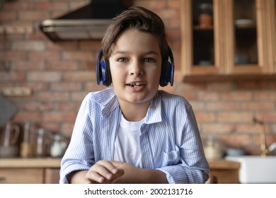 Portrait of cute gen Z school boy in headphones speaking at webcam during video call. Kid learning online, studying from home, using gadget for virtual talk to teacher. Screen view head shot