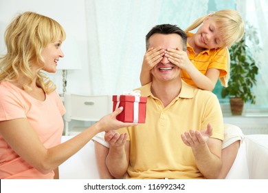 Portrait Of Cute Girl Closing Male Eyes By Hands And Happy Woman Holding Gift For Him