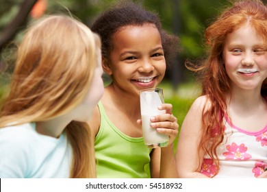 Portrait of cute girl drinking kefir outdoors with her friends near by