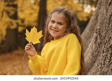 Portrait of cute girl with dry leaf near tree in autumn park - Powered by Shutterstock